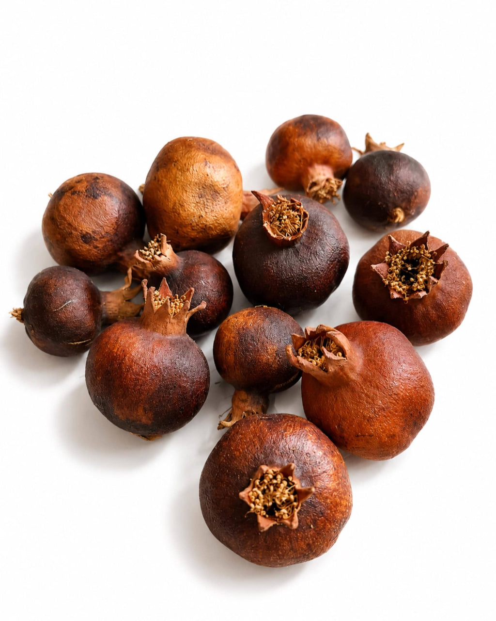 Overhead close-up of small sun-dried pomegranates showing varied shapes and natural gradient tones[span_3](start_span)[span_3](end_span).
