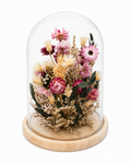 Handcrafted dried flower arrangement in a glass cloche on a light wooden base.
