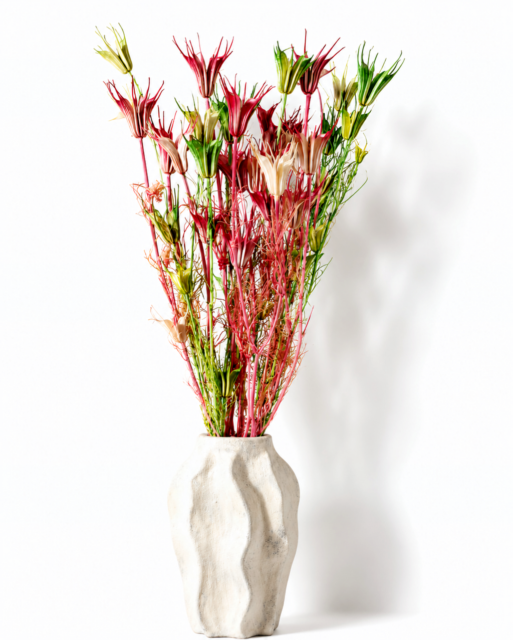 Tall bundle of dried pink and green Nigella stems styled in a textured white ceramic vase.
