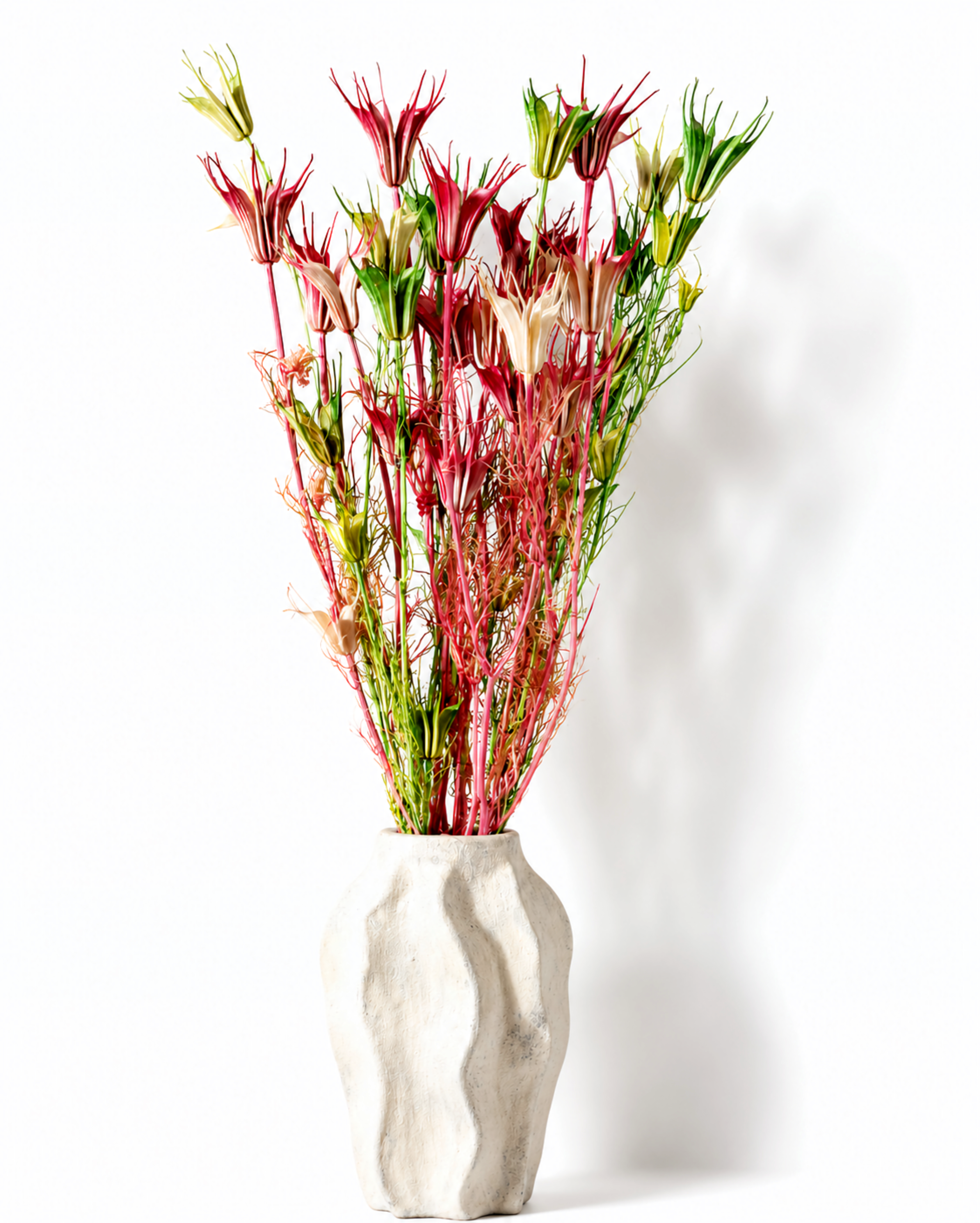 Tall bundle of dried pink and green Nigella stems styled in a textured white ceramic vase.

