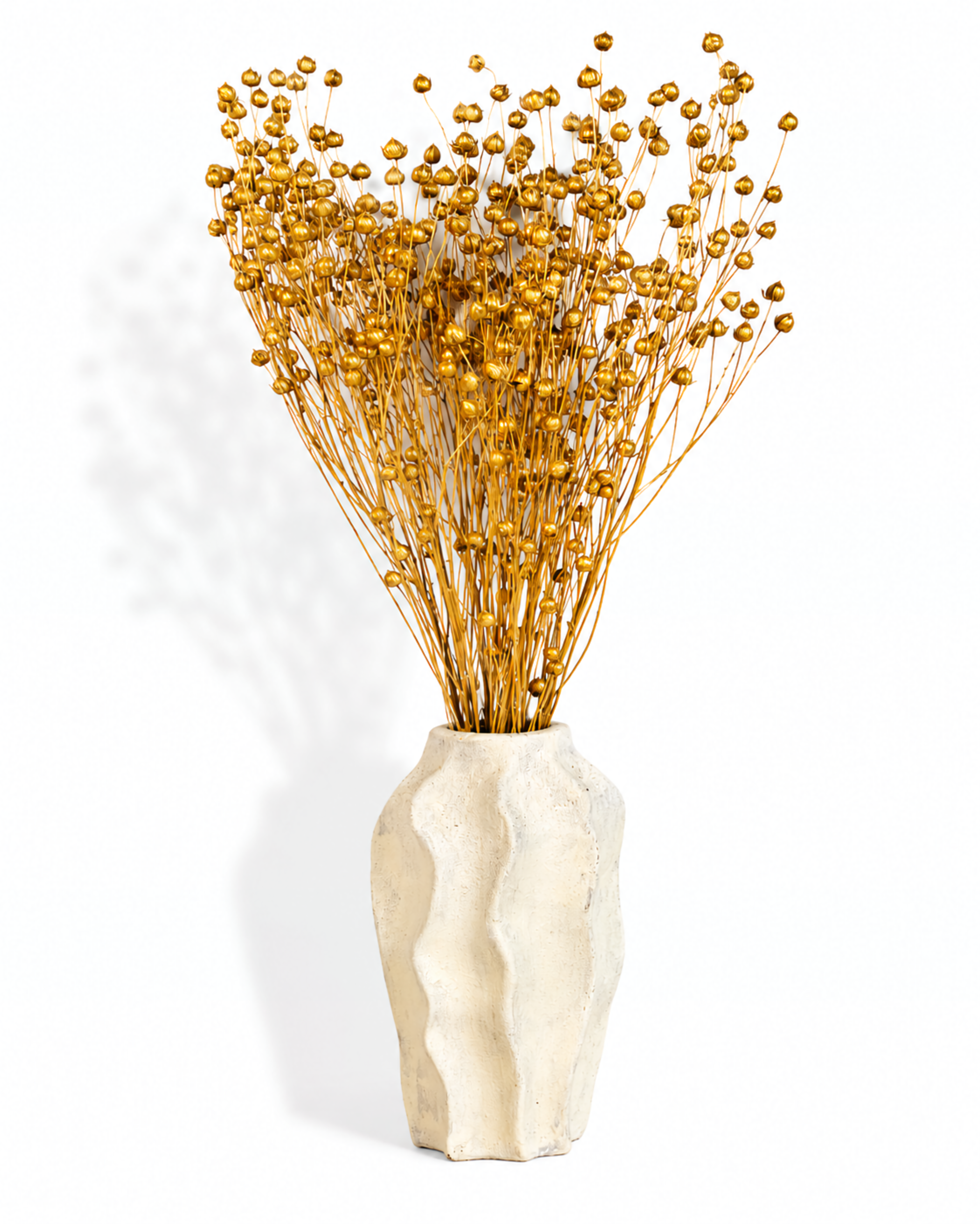 Metallic gold dried flax arrangement displayed in a textured cream ceramic vase against a plain white backdrop.
